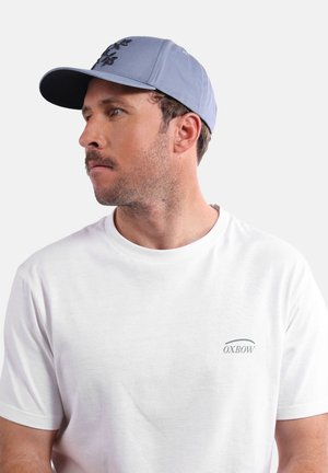 Casquette bleu clair avec une visière courbée et des accents brodés, associée à un t-shirt blanc uni à manches courtes avec un petit logo.