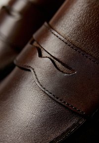 Brązowe skórzane buty o teksturowanym wykończeniu, z przeszywanymi akcentami i falistym zapięciem. Zbliżenie podkreśla detale materiału.
