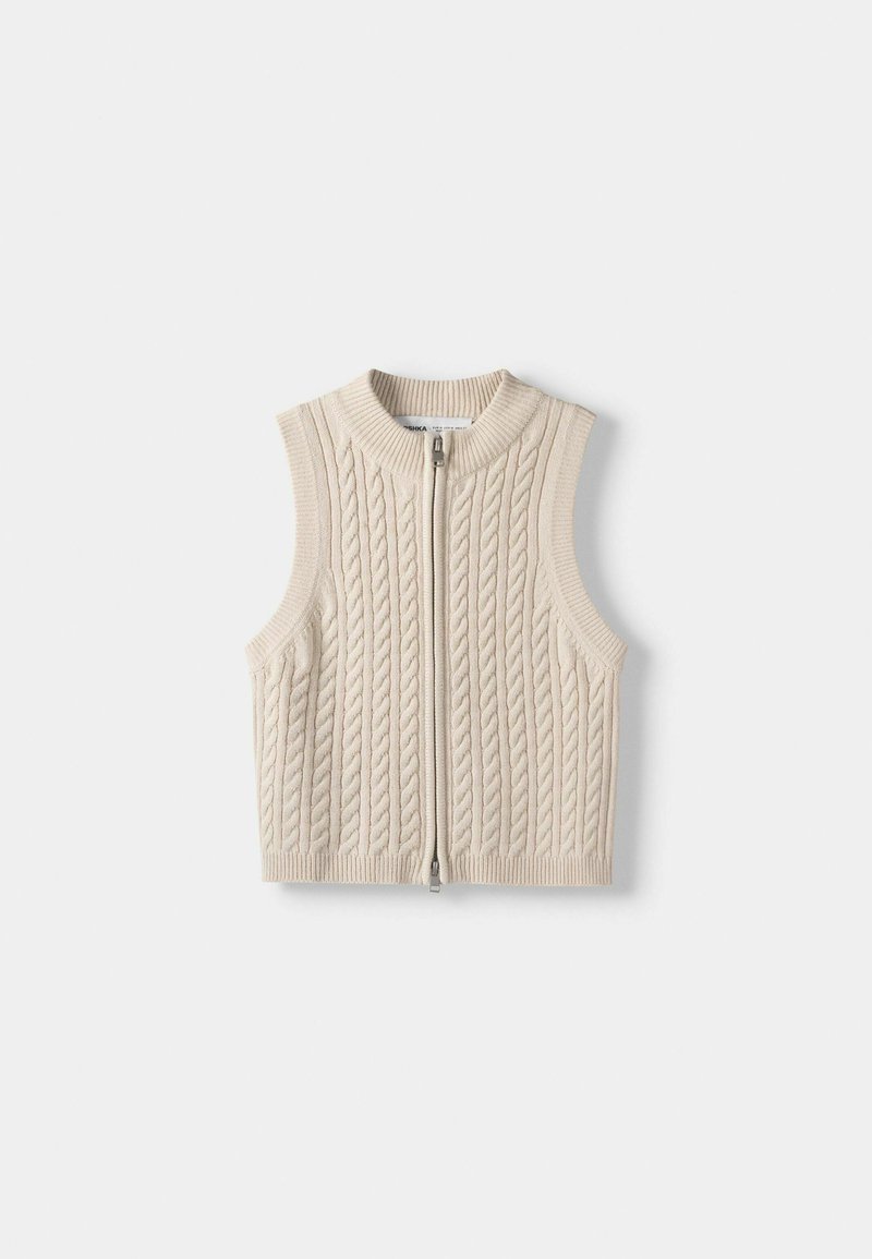 Gilet lavorato a maglia beige con motivo a trecce, design senza maniche, colletto alto e zip anteriore. Il materiale sembra morbido e strutturato.