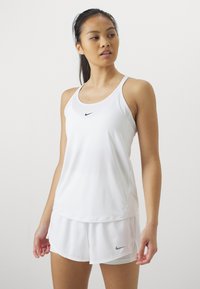 Top deportivo blanco con tirantes delgados, con un pequeño logo negro de Nike en el pecho. Acompañado de pantalones cortos blancos a juego.
