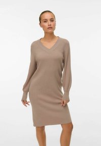 Robe en tricot d'un beige doux avec un décolleté en V et des manches longues, présentant une silhouette ajustée et une texture côtelée sur l'ensemble.