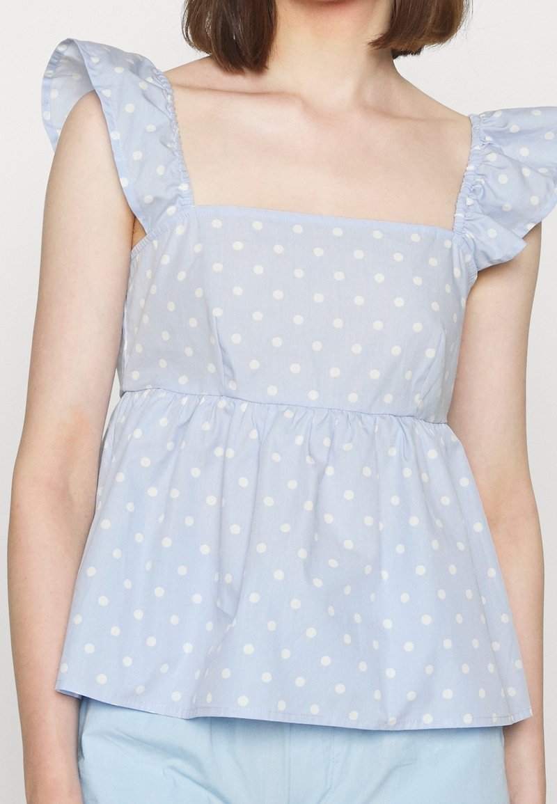Femme portant un haut sans manches bleu clair à pois blancs avec des bretelles à volants, assorti à un bas bleu clair.