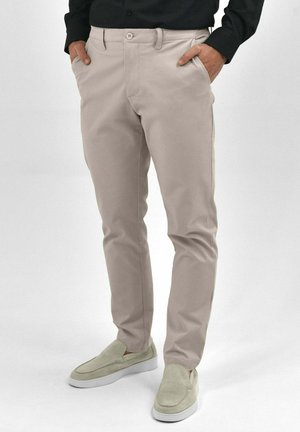 Beige chino's met een slim fit, gekenmerkt door een gladde katoen stof, voorzakken en een knoopsluiting. Gecombineerd met lichtgekleurde loafers.