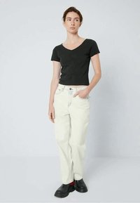 Μαύρο κοντομάνικο μπλουζάκι με V λαιμόκοψη σε συνδυασμό με χαλαρά, ανοιχτόχρωμα μπεζ τζιν. Φορεμένο με μαύρες παντόφλες και κάλτσες με κόκκινες λεπτομέρειες.