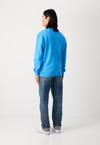 Lichtblauwe sweater met een ronde hals en geribbelde manchetten, gecombineerd met vervaagde blauwe spijkerbroek en witte lage sneakers.
