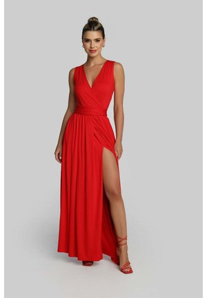 Eine Frau trägt ein ärmelloses rotes Maxikleid mit tiefem V-Ausschnitt und einem Oberschenkelschlitz, kombiniert mit roten, hochhackigen Riemchensandalen.