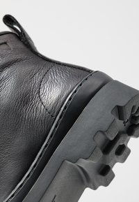 Botte en cuir noir avec dessus texturé, bout rond et semelle en caoutchouc avec des crampons profonds. Inclut une languette au dos pour un enfilage facile.