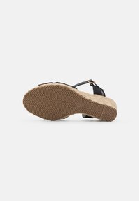 Sandale noire avec une semelle en espadrille texturée, dotée de fines lanières et d'un petit accent de boucle. La semelle présente un motif en zigzag pour une meilleure adhérence.