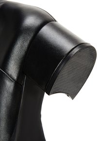 Stivale alla caviglia in pelle nera con tacco tagliato arrotondato e suola in gomma testurizzata. Finitura liscia con dettagli di cucitura minimale.