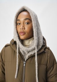 Brown padded jacket with a zip, featuring a light gray textured knitted scarf with drawstrings and a cream high-neck sweater underneath.