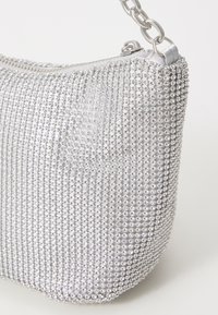 Stříbrná kabelka na večer s kulatým tvarem, vybavená zipovým uzávěrem a řetízkovým popruhem. Povrch je zdoben kruhovými lesklými korálky.