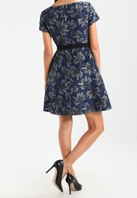 Granatowa sukienka w kwiatowy wzór, krótki rękaw, dopasowana talia, z czarnym paskiem. W połączeniu z czarnymi szpilkami.