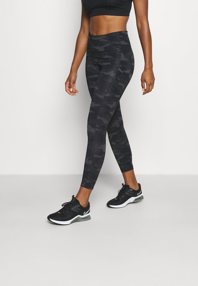 Leggings noirs avec imprimé camouflage et taille haute, présentant une texture lisse et une coupe épurée, associés à des baskets noires à profil bas.