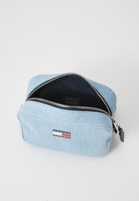 Bolso cosmético de mezclilla azul con cierre de cremallera, forro interior negro y un parche con el logo de Tommy Jeans en la parte frontal.