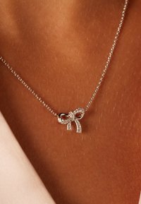 Zilveren ketting met een strik als hanger, gedetailleerd met fonkelende stenen, met een fijne ketting en een gladde, gepolijste afwerking.