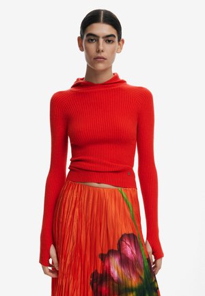 Rotes, geripptes Langarmoberteil mit Kapuze, das eine körpernahe Silhouette und betonte Bündchen aufweist, kombiniert mit einem orangen, plissierten Rock mit Blumenmuster.