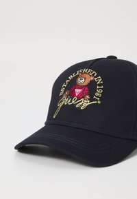 Mørkeblå baseballcap med brodert bjørnelogo, rød skjorte og teksten "Etablert i 1981". Har en strukturert brem og sømdetaljer.