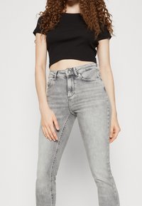 Jeans grises de talle alto con una textura suave, ligero desgastado y cierre delantero de botón, combinados con una camiseta negra de tejido acanalado y corte corto.
