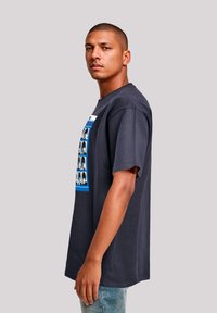 Navy blue short-sleeve t-shirt with a graphic design featuring portrait photos inside a rectangular blue frame. Cotton material, relaxed fit.