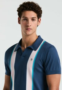 Navyblauwe polo met een textuurafwerking, voorzien van verticale lichtroze en turquoise strepen en een klein pinguïnlogo op de borst.