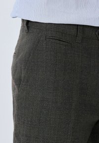 Dunkelkarierte Hose aus strukturiertem Stoff mit Slim-Fit. Verfügt über ein dezentes Karomuster und eine seitliche Tasche.