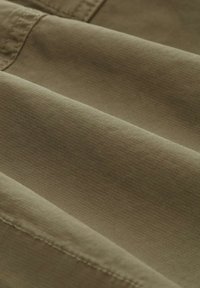 Tkanina w oliwkowym kolorze z teksturowanym, żebrowanym wzorem. Materiał wydaje się miękki i jest złożony, aby pokazać jego kolor i fakturę.