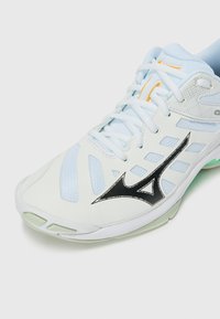 Light blue athletic shoe featuring mesh panels, white synthetic material, black logo accents, and a cushioned sole. Laced design with contrast stitching.