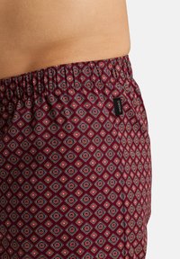 Un short bordeaux à motifs présente un design en diamants avec des accents rouges et bleus, une taille élastique et une petite étiquette de marque.