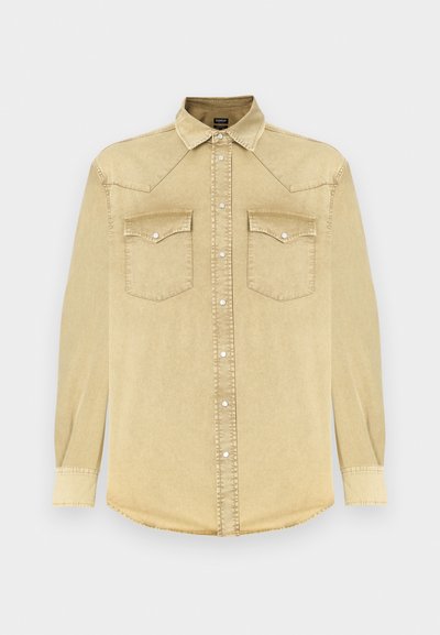 Chemise en denim beige clair à manches longues, col pointu, deux poches poitrine et boutons-pression argentés. Présente un ourlet arrondi et des détails cousus.