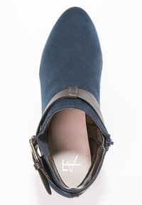 Blå mocka ankelstövel med spetsig tå, brun remdetalj med spänne och en slät inredning. Har en platt klack och minimal sömnad.