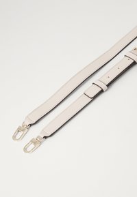 Cinghia per borsa in pelle di un beige chiaro con una trama liscia. Presenta accessori in tonalità oro e lunghezze regolabili con più fori per le adattabilità.