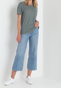Grå t-shirt med et subtilt grønt mønster, parret med lyseblå brede jeans og hvide sneakers. Enkel design, afslappet pasform.