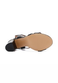 Sandal nero con tacchi alti, punta arrotondata e liscia, cinturini sottili e suola beige testurizzata con scanalature per una migliore presa.
