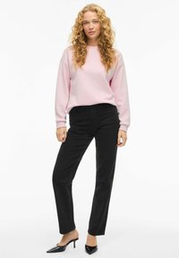 Svetlo roza majica s padlim rameni, v kombinaciji z visokim črnim ravnim hlačami. Črne čevlje s koničastim prstom dopolnjujejo videz.