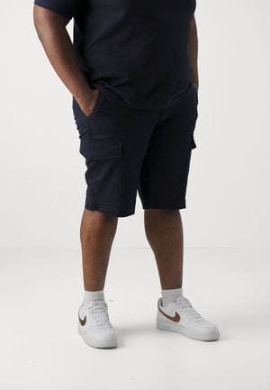 Marine cargoshorts met zijzakken, knielengte ontwerp, gecombineerd met witte sneakers met een metallic accent. Een gladde stoffen textuur.