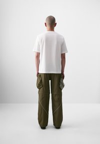 T-shirt en coton blanc et pantalon cargo olive ample avec de grandes poches latérales et des coutures contrastantes, vus de dos sur fond uni.