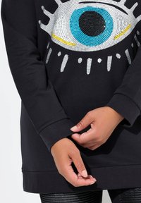 Zwarte sweatshirt met een groot oogontwerp van rhinestones in zilver, blauw, zwart en geel. Strakke ribgebreide manchetten en zoom. Geweven stof.