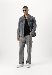 Chaqueta de mezclilla gris con dos bolsillos en el pecho, combinada con pantalones de mezclilla gris a juego. Zapatillas blancas y gafas de sol complementan el conjunto.