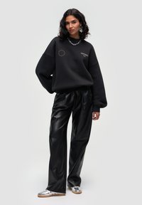 Black oversized sweatshirt with graphic detail, paired with high-waisted black faux leather pants and shiny silver footwear.