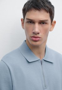 Lyseblå zip-up polo skjorte med blød tekstur, der har en spids krave og en slim fit design. Enkel og minimalistisk look.