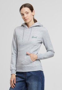 Sudadera de felpa gris con bolsillo canguro, capucha ajustable con cordón y bordado en verde "bosque" en el pecho. Textura suave.