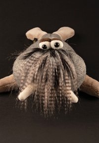 Gray plush toy with large googly eyes, beige ears, and long, striped fur resembling whiskers or a beard against a dark background.