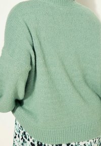 Morbido maglione verde menta oversize con orlo a coste e spalle scese, indossato sopra una gonna a motivi nera, bianca e teal.