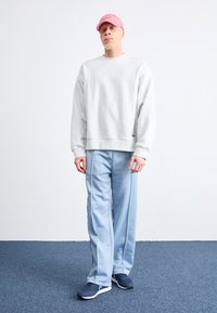 Grå sweatshirt, ljusblå träningsbyxor, marinblå sportskor, rosa keps. Lätt avslappnad passform med ribbad mudd och nederkant, sidostråk på byxorna.