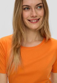 Oranje t-shirt met een ronde hals, gemaakt van zacht materiaal. Het ontwerp heeft korte mouwen en een gladde textuur.