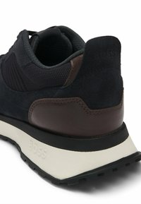 Sneaker nera e blu con tomaia in suede e mesh, dettagli in pelle marrone, suola ammortizzata e branding "BOSS" sul tallone.