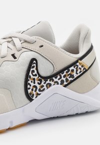 Beige athletic shoe with a textured upper, black accents, and a leopard print swoosh in beige, black, and gold. White rubber sole with Nike branding.