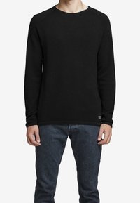 Svart långärmad crewneck sweatshirt i mjukt tyg, med ribbad nederkant och åtsittande ärmslut. Matchad med mörkblå jeans.