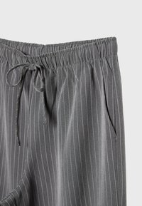 Pantalon gris à fines rayures avec taille élastique et cordon de serrage, doté de poches latérales et d'une texture de tissu douce.