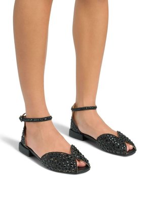 Ballerines noires à bout ouvert avec une bride réglable à la cheville, présentant une tige texturée ornée de petites gemmes noires et des talons plats.